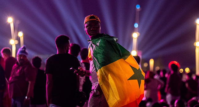 A football fan wears a Cameroon national flag on his back as others gather to watch the Group A match between Qatar and Ecuador as they attend the FIFA Fan Festival at Al Bidda park in Doha on November 20, 2022, on the opening of the Qatar 2022 World Cup football tournament. (Photo by Philip FONG / AFP)