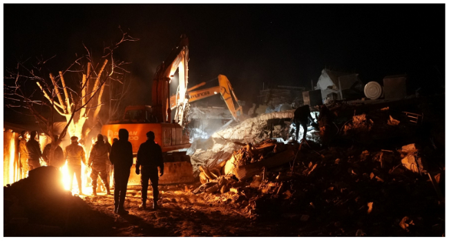 Rescue workers rest by a fire as others continue to dig through the rubble of a building in the rebel-held town of Jindayris on February 8, 2023, two days after a deadly earthquake that hit Turkey and Syria. (Photo by Rami al SAYED / AFP)