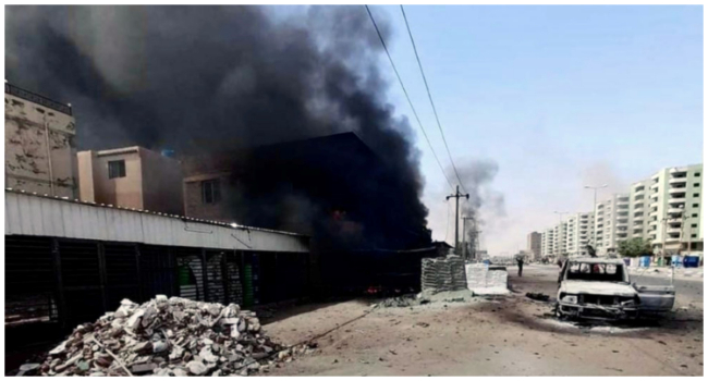 This handout photo taken on April 23, 2023 and released on April 24 by the Indonesian Foreign Ministry shows smoke rising from a building next to a damaged car on a street in Khartoum. (Photo by Handout / INDONESIAN FOREIGN MINISTRY / AFP)