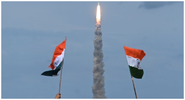 People wave Indian flags as an Indian Space Research Organisation (ISRO) rocket carrying the Chandrayaan-3 spacecraft lifts off from the Satish Dhawan Space Centre in Sriharikota, an island off the coast of southern Andhra Pradesh state on July 14, 2023. (Photo by R.Satish BABU / AFP)