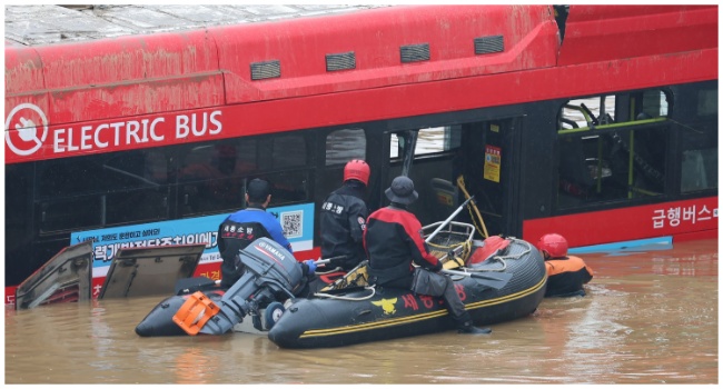 South Korean rescue workers search for missing persons near a bus along a deluged road leading to an underground tunnel where some 15 cars were trapped in flood waters after heavy rains in Cheongju on July 16, 2023. (Photo by YONHAP / AFP)