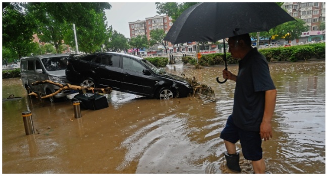 A man wades past a damaged car along a flooded street, after heavy rains in Mentougou district in Beijing on July 31, 2023. (Photo by Pedro PARDO / AFP)