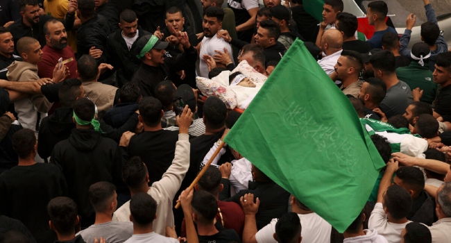 A Palestinian man waves a Hamas flag as mourners carry the body of Palestinian protester Muhammed Jawad Zughayer, 21, who was killed in clashes with Israeli forces the previous night in Hebron, during his funeral in the southern West Bank city on October 9, 2023.