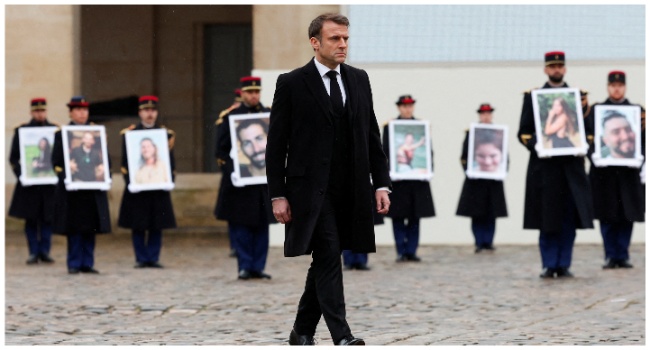French President Emmanuel Macron (C) walks in front of members of the French Republican Guard (Garde Republicaine) holding portraits of the 42 French and French-Israeli citizens killed, during a ceremony to pay tribute to the French victims of the attack by Hamas against Israel on October 7, at the Invalides memorial complex in Paris, on February 7, 2024. (Photo by GONZALO FUENTES / POOL / AFP)