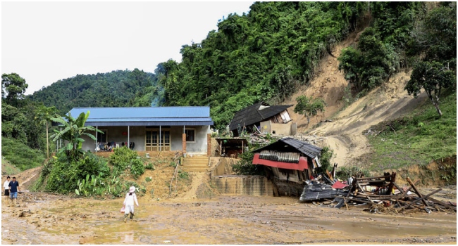 People walk through the mud past the debris of damaged property in the aftermath of a landslide triggered by heavy rains in Vietnam's Dien Bien province © Hoang Bon / AFP