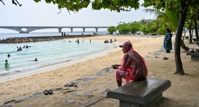 A man sits under a tree as it rains at Artificial Beach in Malé on May 15, 2026