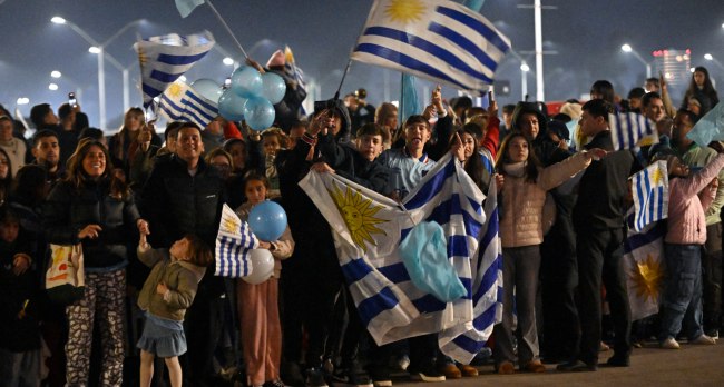 Fans-wave-flags-while-waiting-for-the-arrival-of-Uruguays-national-football-team-at-Carrasco-Intern Thousands Of Protesters Block Road To World Cup Stadium
