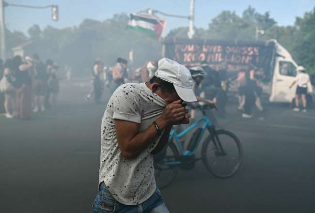 A demonstrator puts his face in his t-shirt as he reacts to tear gas during a rally of a "No-G7" coalition of over 60 associations, unions and left-wing groups "against fascism and imperialism”, a day ahead of the summit's start, in Geneva on June 14, 2026. (Photo by FABRICE COFFRINI / AFP)