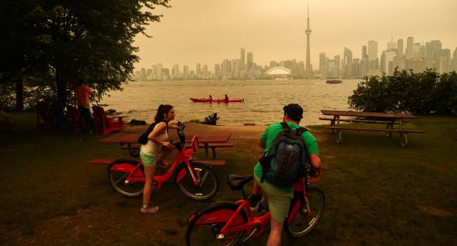 People pause as they cycle on the Toronto Islands as forest fires in Northern Ontario cause poor air quality over the city, in Toronto, Ontario, Canada, July 15, 2026. (Photo by COLE BURSTON / AFP)